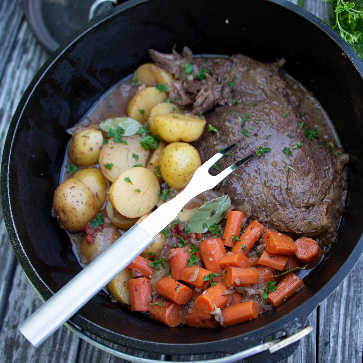 Handcrafted Rada carving fork with long stainless steel tines resting in a cast iron Dutch oven with cooked beef, carrots, and baby potatoes, ideal for Kitchen & Food, Storage and Serving, USA Made, Best Sellers, and Promo Eligible collections.