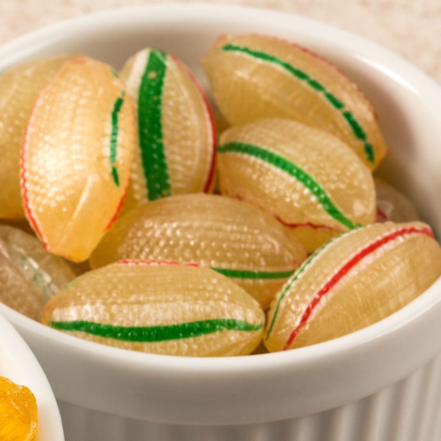 Close-up of handcrafted hard mints with green and red stripes in a white ceramic dish, showcasing a cool peppermint flavor ideal for kitchen, snacks, and USA made collections.