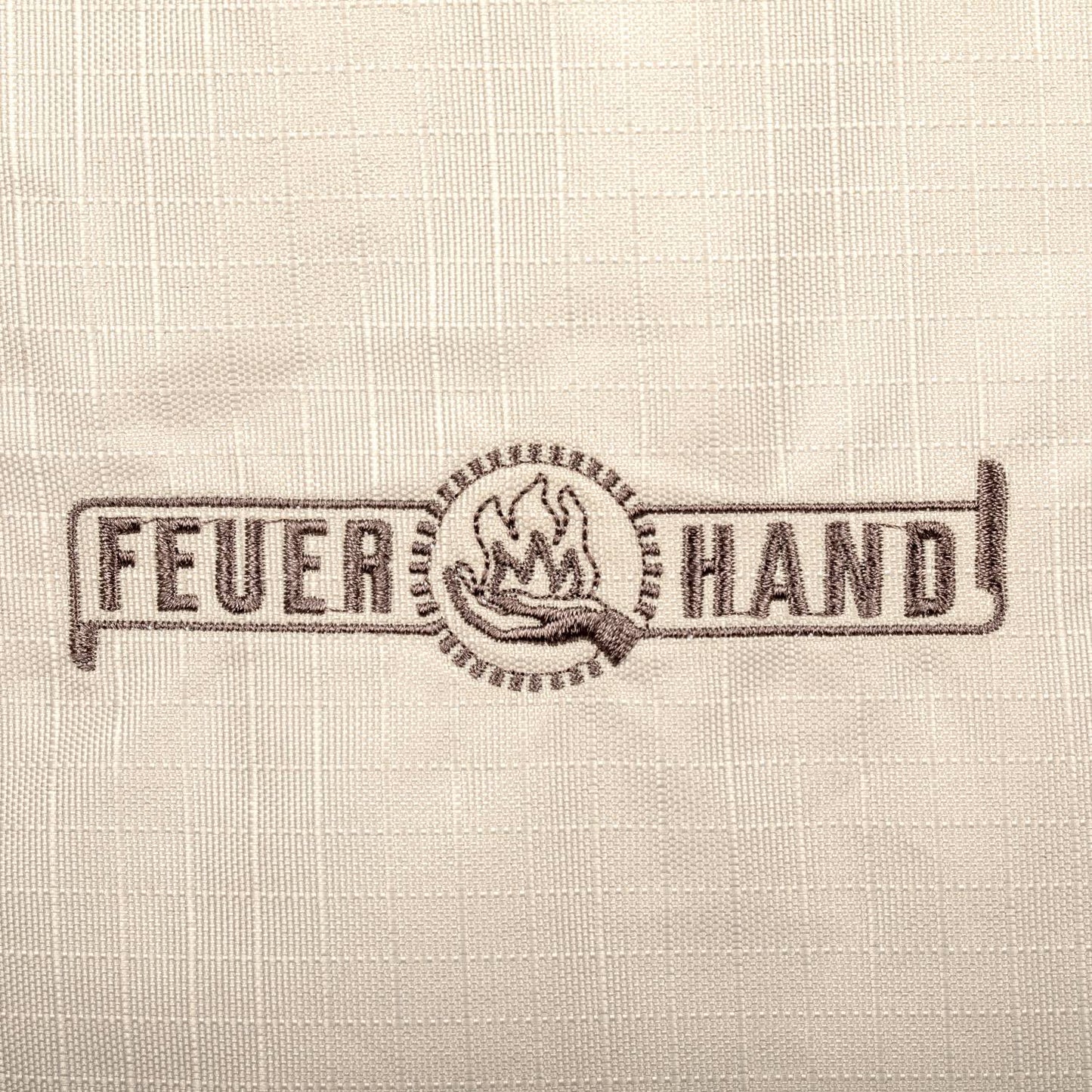 Close-up of the Feuerhand logo embroidered on weather-resistant ripstop fabric in light beige, featured in Farm, Garden & Tool and Camping collections.