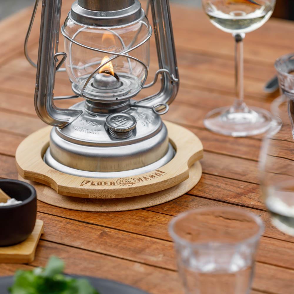 Circular bamboo oil lantern coaster with an engraved logo, designed to protect wooden surfaces from oil spills, featuring indentations for secure lantern placement, ideal for camping and emergency use.