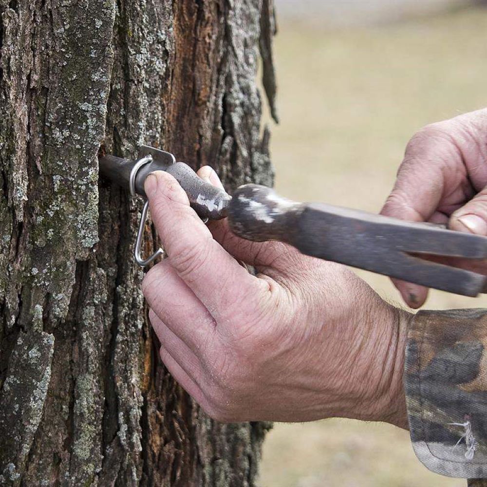 Close-up of hands using a handcrafted solid cast iron spout driver to tap a metal spout into a tree, featured in Farm, Garden & Tool and Maple Syrup Sugaring Supplies collections.