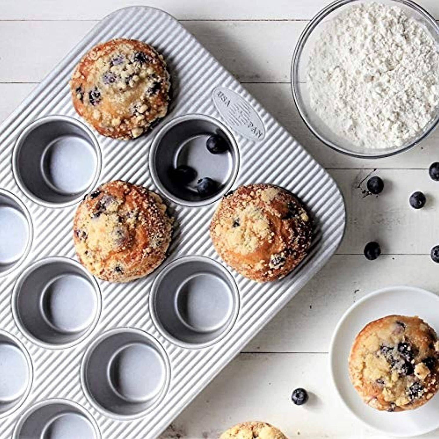 Handcrafted non-stick muffin pan with 12 fluted cups for even baking, made in USA, shown with freshly baked blueberry muffins and baking ingredients, ideal for Kitchen & Food and Baking Supplies collections.