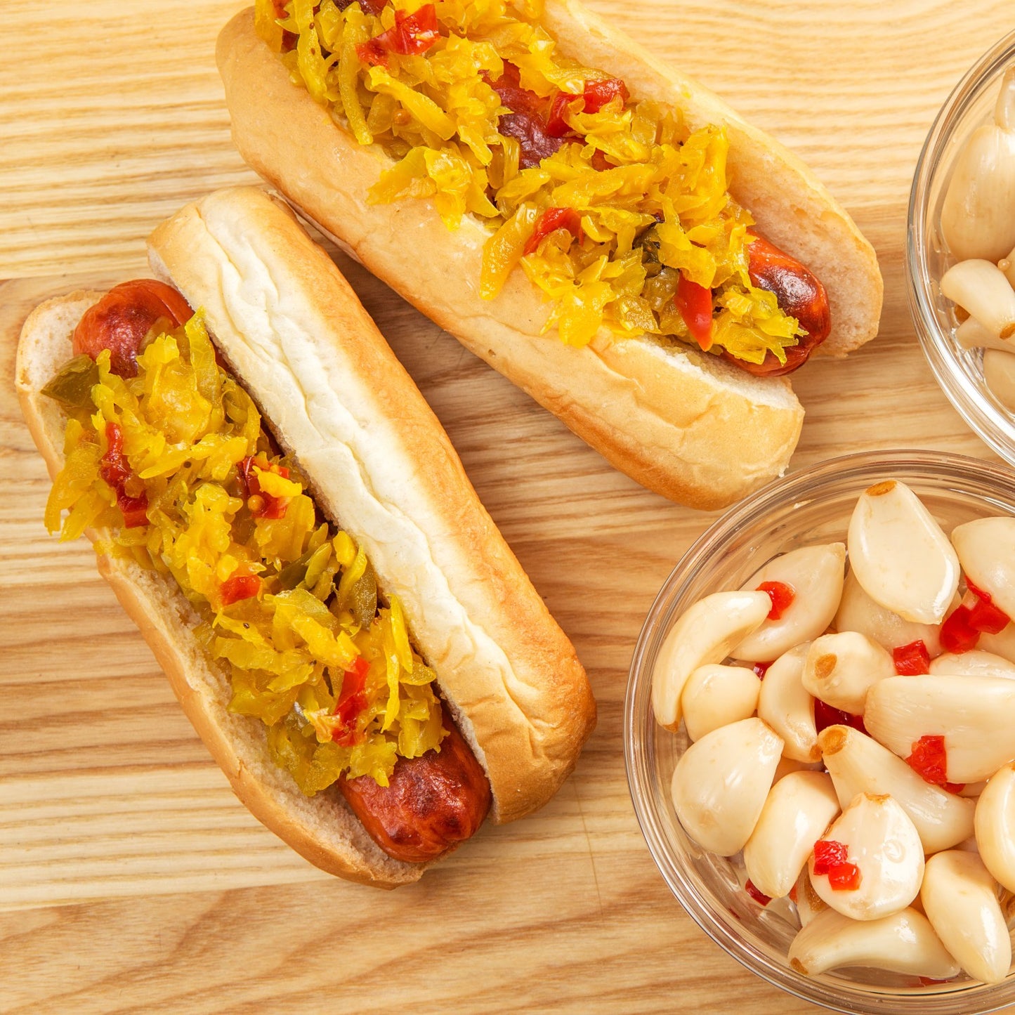 Two grilled hot dogs topped with spicy Southern Chow-Chow relish on soft buns, accompanied by a bowl of pickled garlic with red pepper, ideal for Kitchen & Food, Pantry, USA Made, Best Sellers, and Promo Eligible collections.