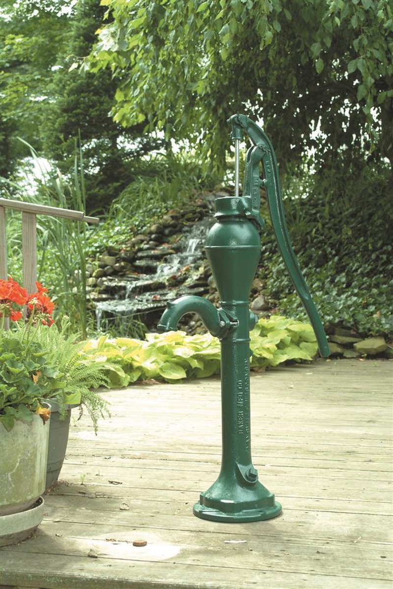 Green cast iron deep well pump head with long lever handle mounted on wooden deck near vibrant garden plants and a small cascading rock waterfall, featured in Appliances, USA Made, Water Pumps, Deep Well Pumps, Best Sellers, Promo Eligible, and All Stoves & Appliances collections.