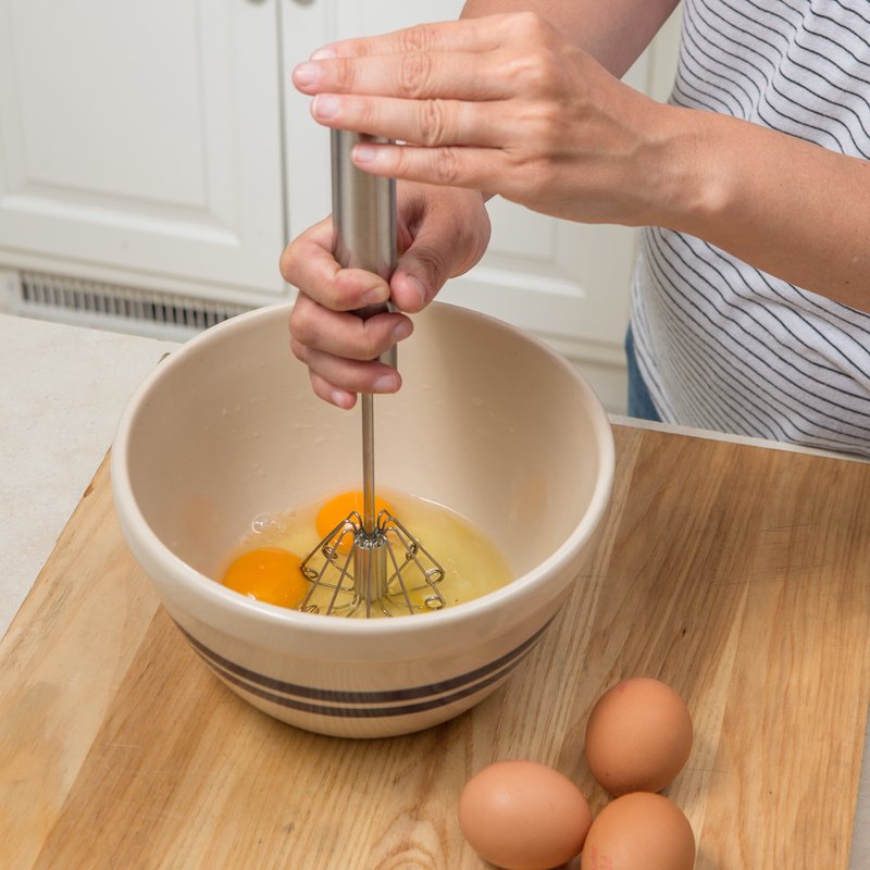 Hand using a stainless steel whisk to blend eggs in a ceramic mixing bowl on a wooden countertop, suitable for Kitchen & Food, Kitchen Gadgets, Cooking and Baking Helpers, Best Sellers, and Promo Eligible collections.