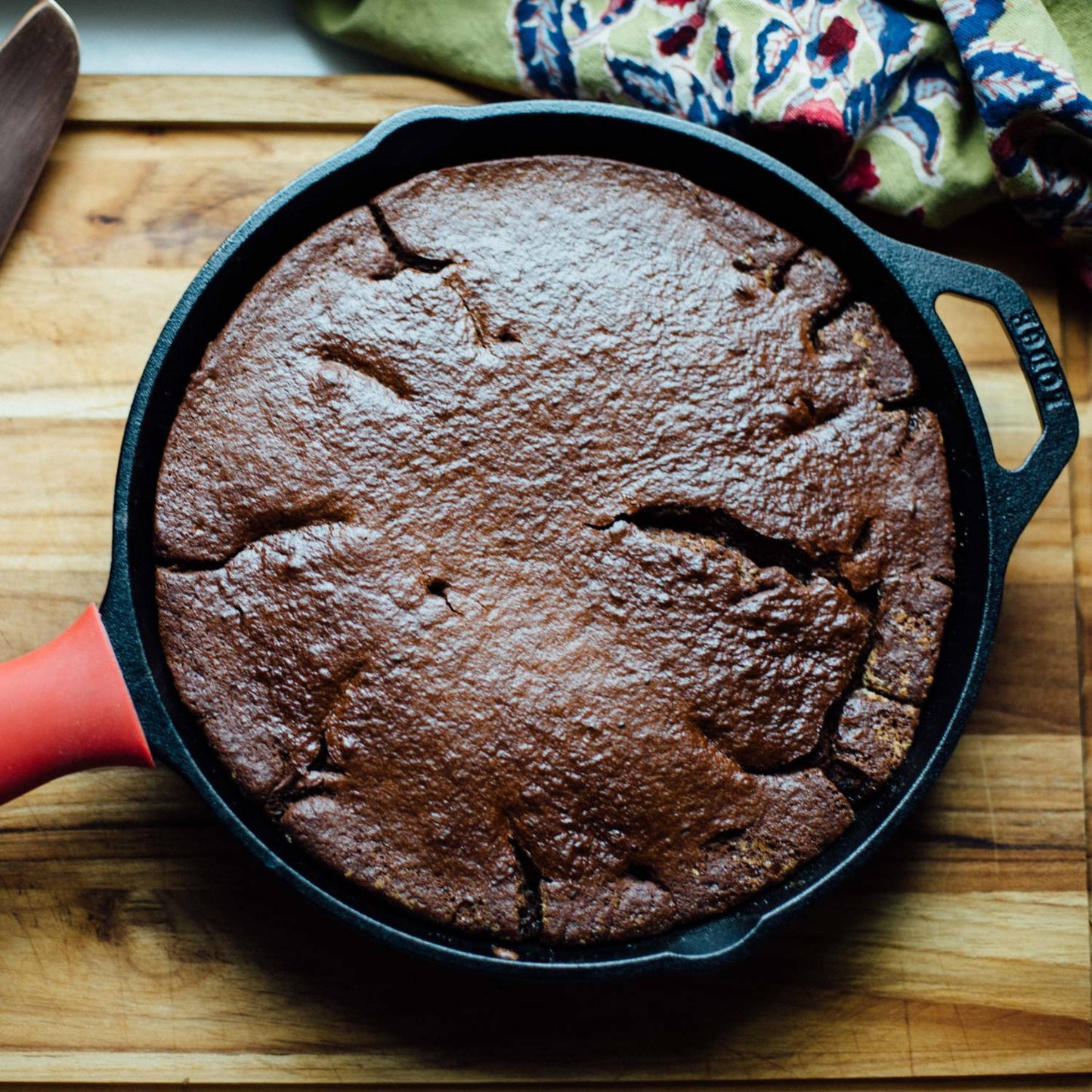 Handcrafted pre-seasoned cast iron skillet with a red silicone handle grip, freshly baked chocolate cake inside, showcasing exceptional heat retention and durability for Kitchen & Food, Cookware, Cast Iron, Best Sellers, Promo Eligible collections.