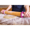 Beechwood adjustable rolling pin with removable thickness discs in pink and white, used to roll dough on a floured surface, ideal for baking and kitchen tasks.