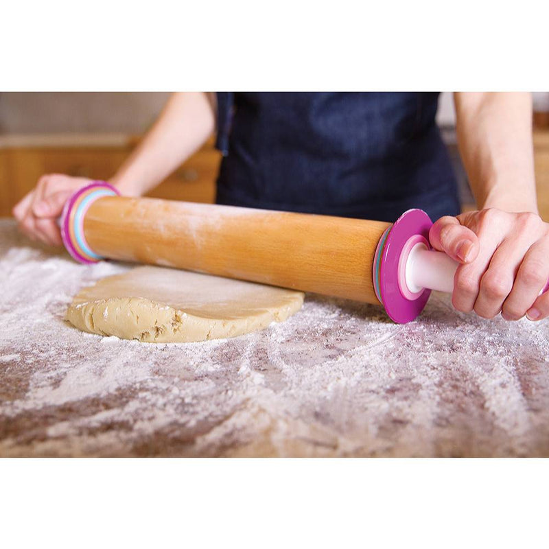 Beechwood adjustable rolling pin with removable thickness discs in pink and white, used to roll dough on a floured surface, ideal for baking and kitchen tasks.