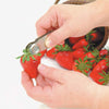 Sturdy stainless steel strawberry huller removing hull from fresh berry, held over basket of ripe strawberries, ideal for Kitchen & Food, Specialty Equipment, Peelers and Pitters, and Best Sellers collections.