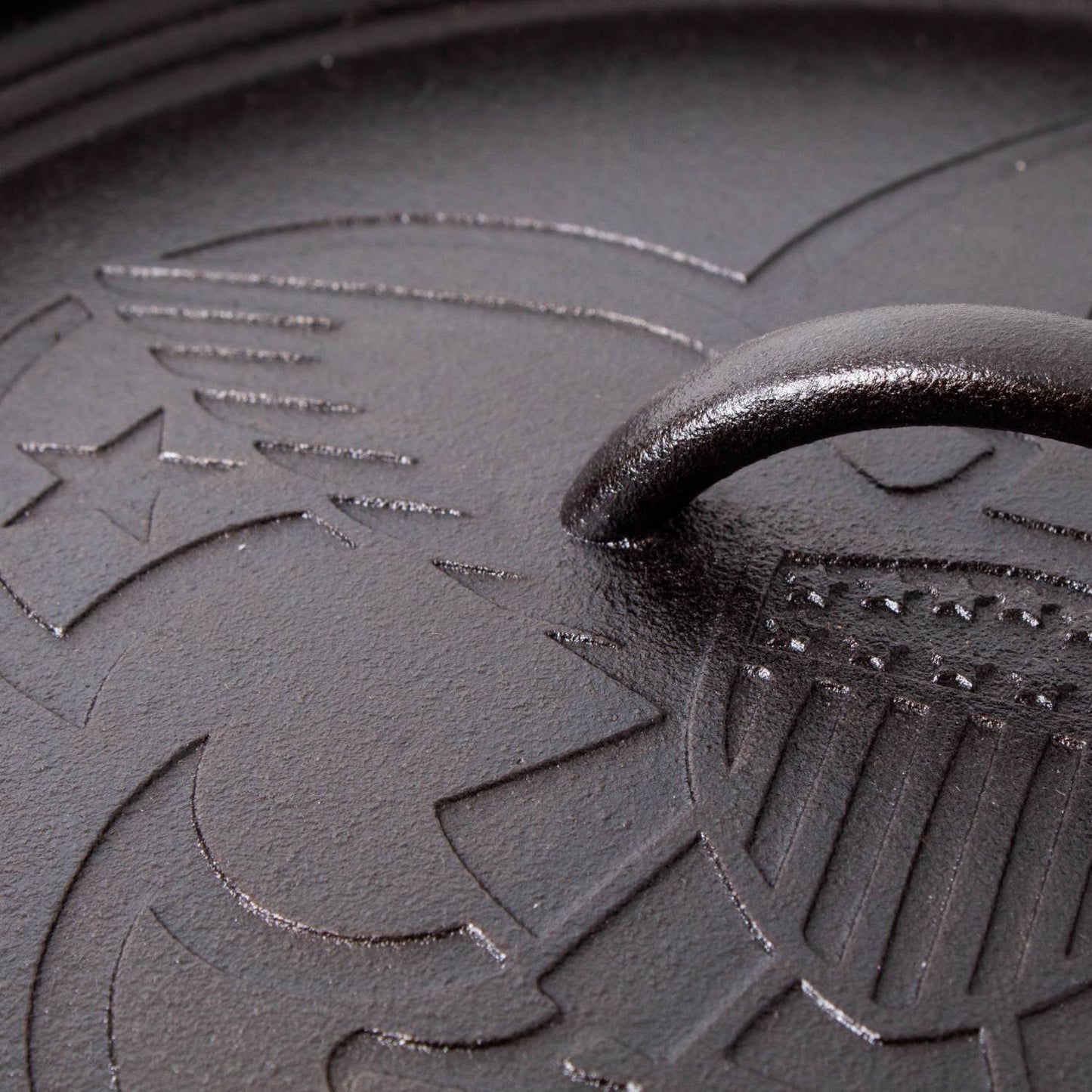 Close-up of a cast iron lid featuring embossed Boy Scout emblem details on a seasoned surface, highlighting durable craftsmanship in USA made cookware for camping and kitchen use.