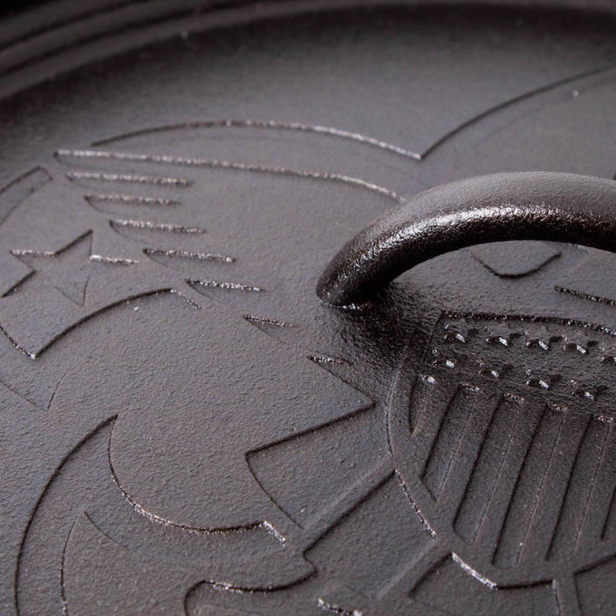 Close-up of a cast iron lid featuring embossed Boy Scout emblem details on a seasoned surface, highlighting durable craftsmanship in USA made cookware for camping and kitchen use.