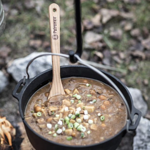 Outdoor cast iron pot with flat base filled with hearty stew garnished with chopped green onions and mushrooms, featuring a wooden branded spatula, Kitchen & Food, Cookware, Cast Iron, Best Sellers, Promo Eligible collections.
