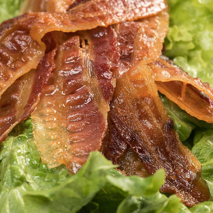 Close-up of crispy cooked bacon strips resting on fresh green lettuce, showcasing a savory, ready-to-eat meat option ideal for Kitchen & Food, Camping, and Emergency Supplies collections.