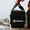 Person holding a black reinforced transport bag with shoulder strap, designed for outdoor stove carrying, featuring water-repellent ripstop fabric, ideal for camping and farm use.