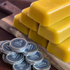 Stacked yellow beeswax blocks alongside several small silver tins of cast iron seasoning, displayed on a wooden surface for Kitchen & Food, Cookware, Cast Iron, USA Made, and Best Sellers collections.