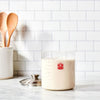 Clear glass sourdough crock filled with bubbly starter, accompanied by a stainless steel lid and wooden spoons in a ceramic holder, ideal for Kitchen & Food, Cookware, Baking Supplies, and Storage collections.