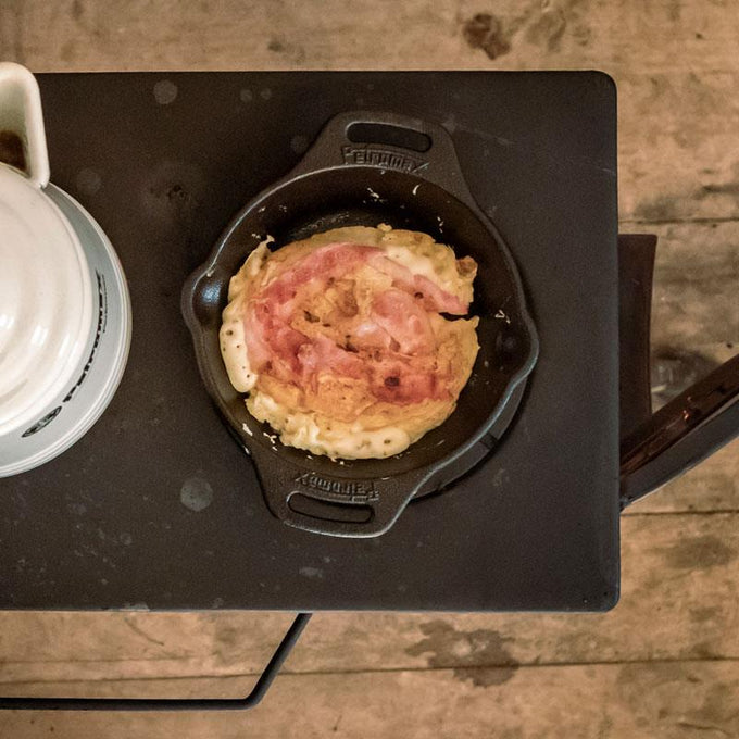 Top view of a heavy-duty cast iron skillet with two side handles cooking an omelet topped with bacon, perfect for farm, kitchen, camping, and cookware collections.