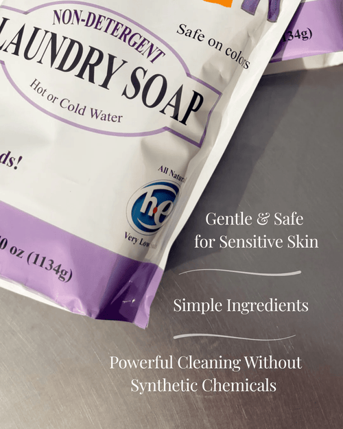 Partial view of a lavender and white package of non-detergent laundry soap featuring benefits for sensitive skin, simple natural ingredients, and powerful cleaning without synthetic chemicals, ideal for laundry supplies and soapmaking collections.