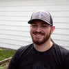 Man wearing a handcrafted Lehman's embroidered trucker hat with a grey front panel, black stretch mesh back, and slight pre-curved visor, featured in Health & Wellness and Best Sellers collections.