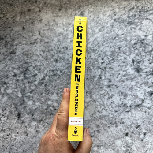 Hand holding the spine of a brightly colored yellow book titled with bold black text, part of Books, Farm and Livestock Books, Chicken Accessories, and Best Sellers collections.
