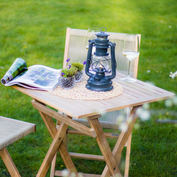 Handcrafted dark galvanized oil lantern with thermal heat-resistant SUPRAX globe, featured on a wooden outdoor table with wine glasses and a magazine, ideal for camping and outdoor collections.