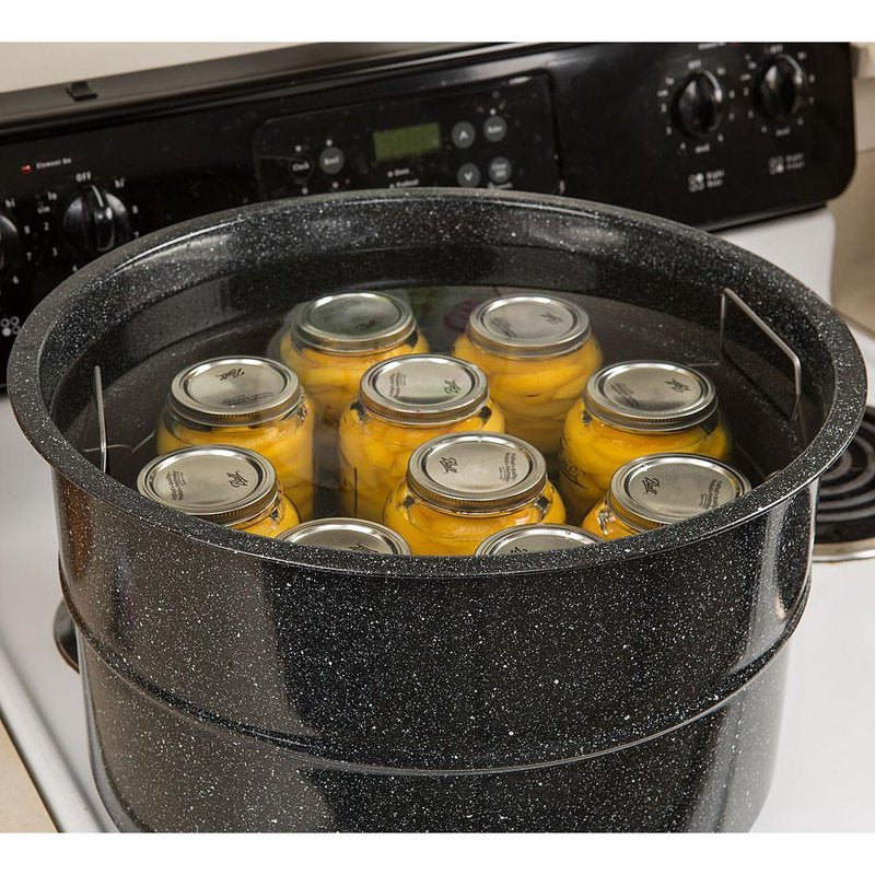 Black speckled enamelware canner on stovetop, filled with glass jars of preserved peaches in water, featuring a metal rack, ideal for water bath canning in Kitchen & Food and Food Preservation collections.