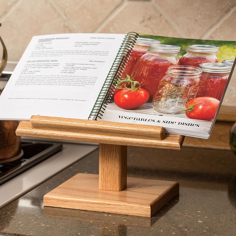Handcrafted solid oak cookbook holder with a clear, smooth finish, displaying an open spiral-bound cookbook with tomato preserves, featured in Kitchen & Food, Kitchen Gadgets, Amish Made, and USA Made collections.