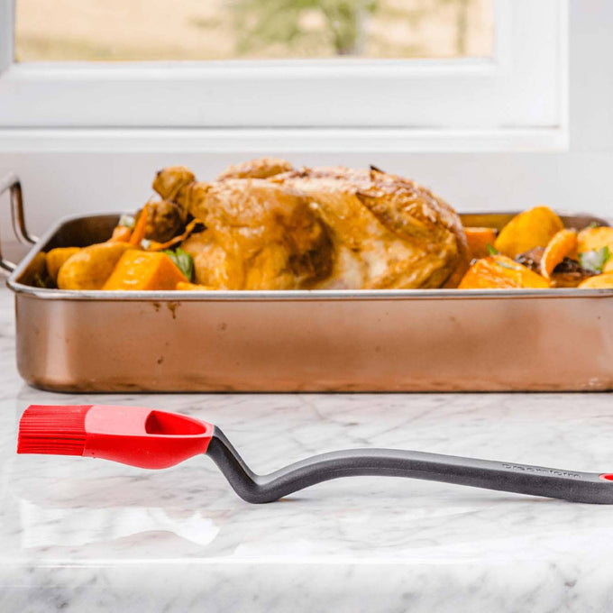 Silicone basting brush with angled black handle and red flexible head designed to reach tight spaces for basting roasted chicken and vegetables, perfect for Kitchen Gadgets and Grilling collections.