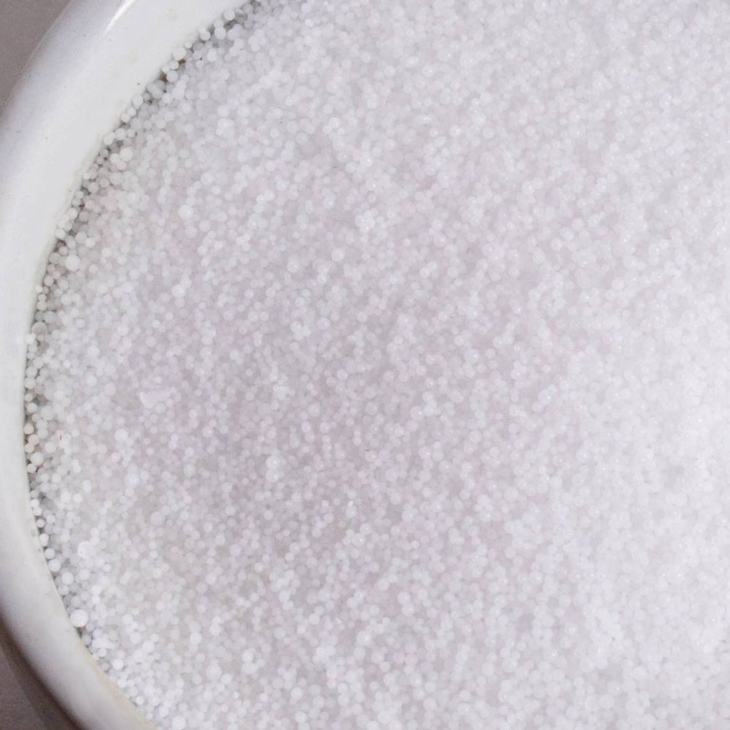 Close-up view of small, white, food-grade sodium hydroxide lye beads in a ceramic container, ideal for soapmaking and featured in Health & Wellness and Soapmaking Supplies collections.