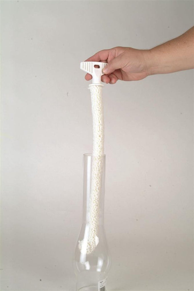 Hand holding a flexible white foam brush with a plastic handle, cleaning inside a clear glass oil lamp chimney, showcasing durable and soft design made in USA for lamps and lighting care.