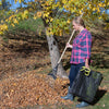 Person using a rake to gather fallen leaves next to a tree, holding a black woven polyethylene Clean Up Canvas with reinforced yellow soft grip handles, ideal for Farm, Garden & Tool and Lawncare collections.