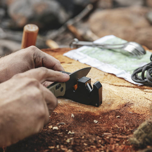 Person sharpening a folding knife with a compact black and yellow handheld sharpener on a wooden surface, ideal for Farm, Garden & Tool, Kitchen & Food, Knives & Axes, and Sharpening collections.