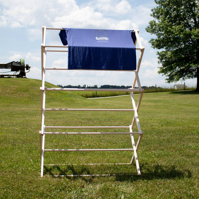 Handcrafted small wooden floor clothes dryer standing outdoors on a grassy field, holding a blue garment, highlighting Amish made, USA made, and best sellers in Home & Decor and Laundry Supplies collections.
