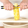 Two hands gripping a yellow-handled corn stripper removing kernels from an ear of corn positioned over a wooden board and beige ceramic bowl, ideal for Kitchen & Food, Food Prep, Choppers and Cutters, Food Preservation, Freezing, Best Sellers, and Promo Eligible collections.