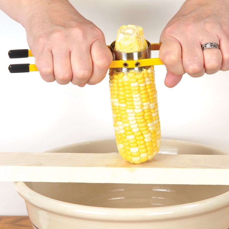Two hands gripping a yellow-handled corn stripper removing kernels from an ear of corn positioned over a wooden board and beige ceramic bowl, ideal for Kitchen & Food, Food Prep, Choppers and Cutters, Food Preservation, Freezing, Best Sellers, and Promo Eligible collections.