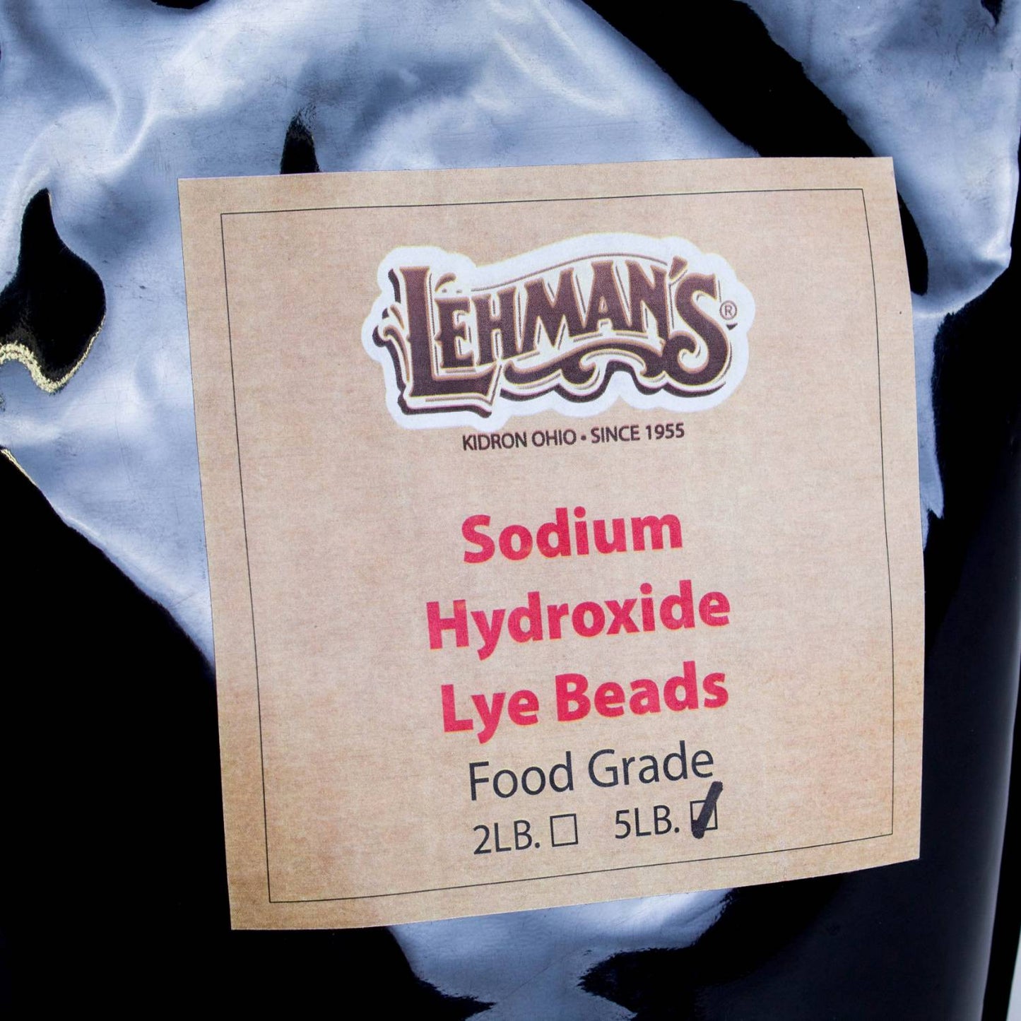 Close-up of a kraft paper label on a resealable black pouch indicating food-grade sodium hydroxide lye beads in a 5-lb size, featured in Health & Wellness, Soapmaking Supplies, USA Made, and Best Sellers collections.
