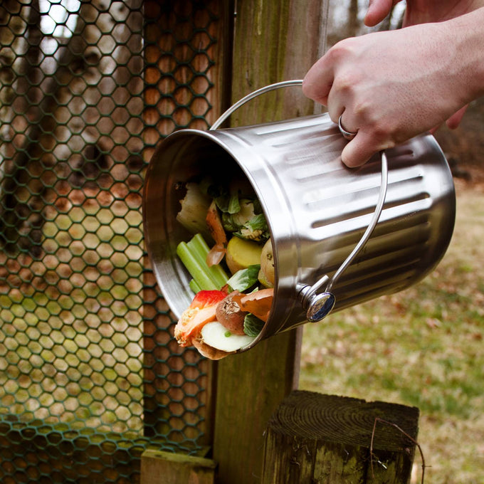 Brushed stainless steel compost pail with sturdy handle being emptied outdoors, designed for odor-free food scrap collection in Farm, Garden & Tool and Kitchen & Food collections.