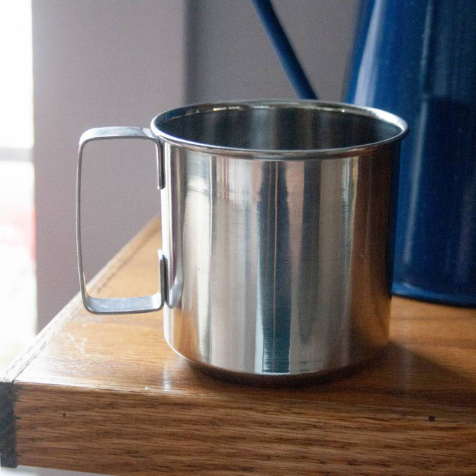 Stainless steel cup with a sturdy handle, placed on a wooden surface, ideal for camping, kitchen use, and outdoor dining in Farm, Garden & Tool, Kitchen & Food, and Camping collections.
