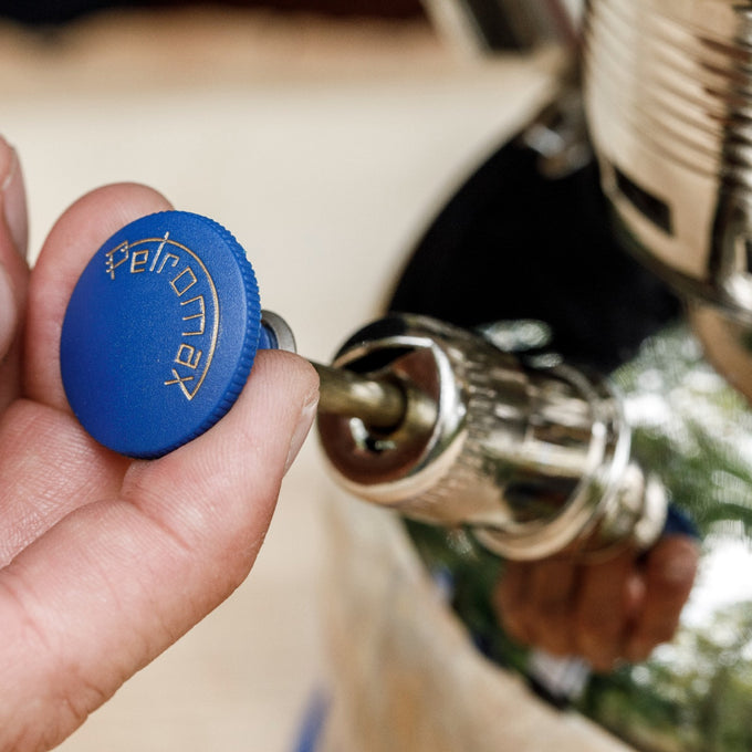 Hand gripping a brass and chrome pump component with a blue knob engraved with Petromax, designed for lamps, featured in Lamps & Lighting, Parts and Accessories, Other Parts, Best Sellers, and Promo Eligible collections.