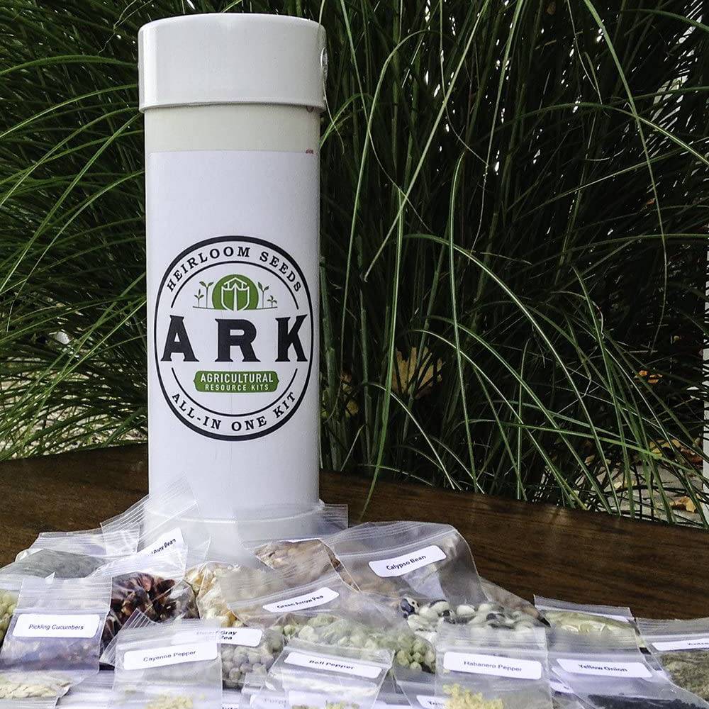 White cylindrical container labeled ARK Agricultural Resource Kits with assorted heirloom seed packets spread on a wooden surface, set outdoors with green foliage, handmade in USA, featured in Farm, Garden & Tool and Seeds and Planting collections.