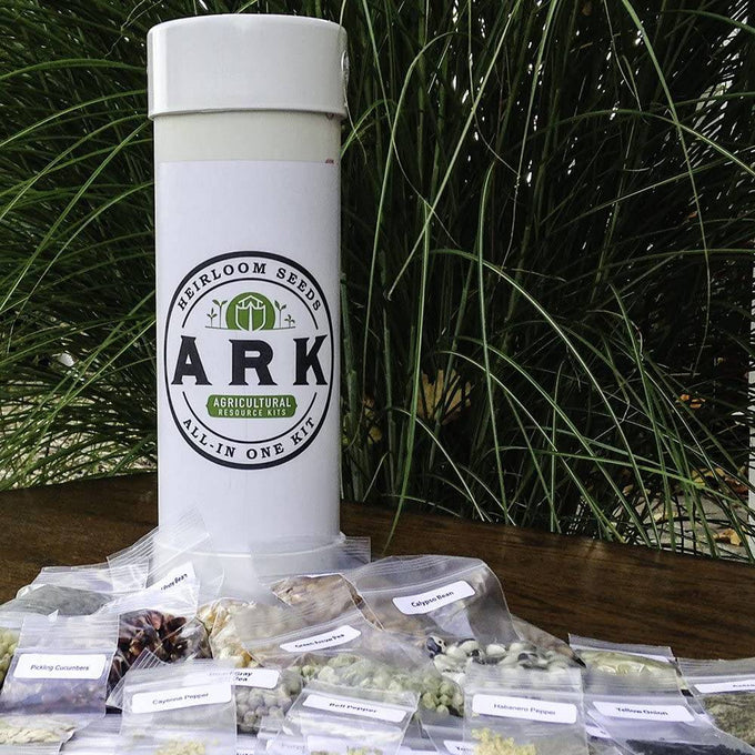 White cylindrical container labeled ARK Agricultural Resource Kits with assorted heirloom seed packets spread on a wooden surface, set outdoors with green foliage, handmade in USA, featured in Farm, Garden & Tool and Seeds and Planting collections.