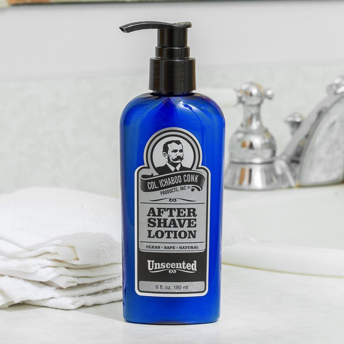 Blue pump bottle of unscented after-shave lotion labeled for natural, gentle skin care, placed on marble countertop near faucet and folded white towels in grooming and personal hygiene setting.