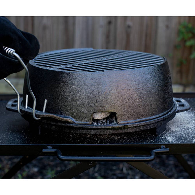 Handcrafted portable cast iron grill with detachable spring handles, heated over charcoal on a sturdy outdoor table, perfect for camping, grilling, and outdoor cooking.