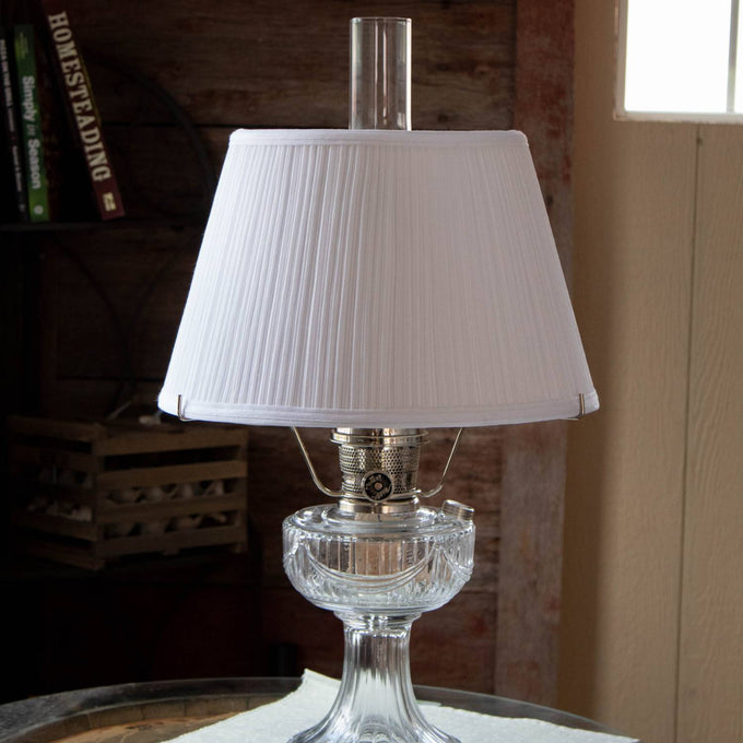 White cloth pleated lamp shade on a classic oil lamp with a clear glass base, highlighting soft, even light diffusion, ideal for lamps & lighting and lamp shade accessories collections.