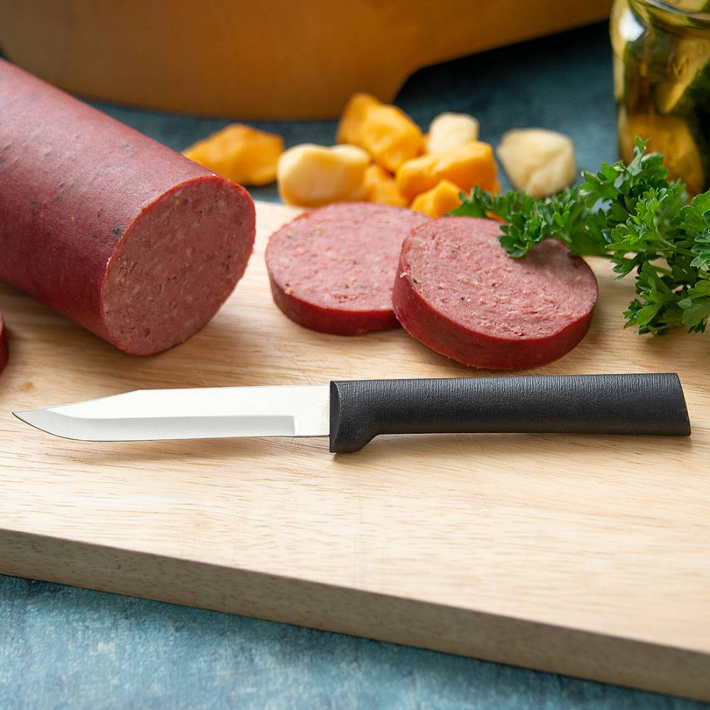 Handcrafted paring knife with a black handle and sharp blade resting on a wooden cutting board, alongside sliced sausage, cheese chunks, and fresh parsley, ideal for kitchen and food prep.