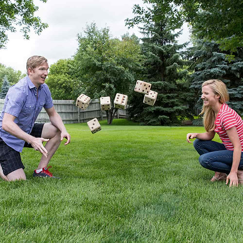 Two people playing with large wooden dice in a grassy backyard, showcasing handcrafted yard dice from the Toys, Books & Games and Lawn Games collections.