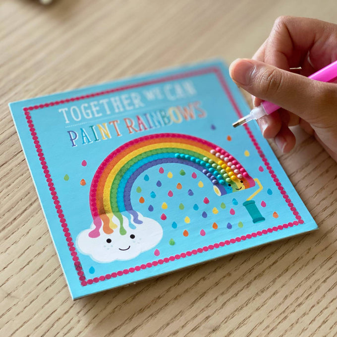 Child's hand using a pink stylus tool to place colorful diamond stones on a handcrafted blue artboard with a smiling cloud and rainbow design, part of Toys, Children's Toys, Arts and Crafts, and Best Sellers collections.