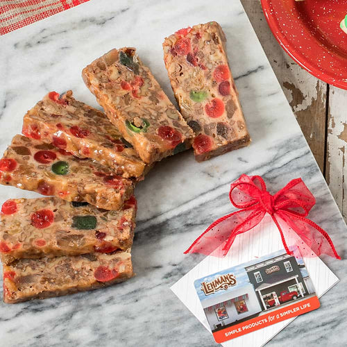 Slices of hand-prepared fruitcake bursting with candied cherries, nuts, and fruit, displayed on marble alongside a festive gift tag, perfect for Kitchen & Food and USA Made collections.