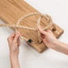 Close-up of hands threading sturdy natural rope through pre-drilled holes of a handmade wooden swing seat, crafted in USA, part of outdoor wooden toys and children's play collections.