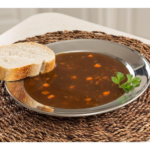 Handcrafted stainless steel soup plate with a wide rim holding vegetable beef soup and a slice of bread, styled on a woven placemat for Kitchen & Food, Dinnerware, and Best Sellers collections.
